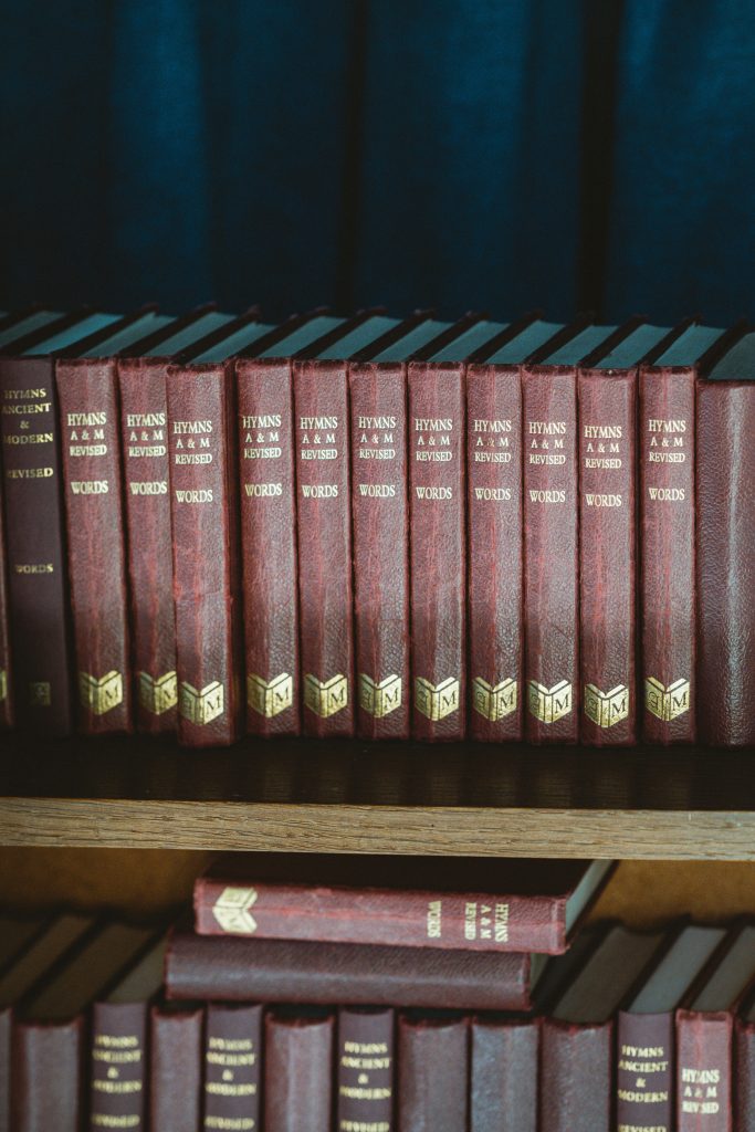Red hardbound hymn books on a wooden shelf